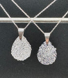 Two silver teardrop pendants on chains against a black background